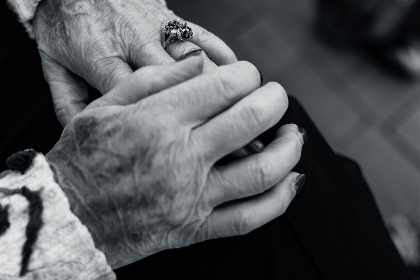 Biography videos Two hands, one older and wrinkled, gently clasping a smaller hand with a ring.