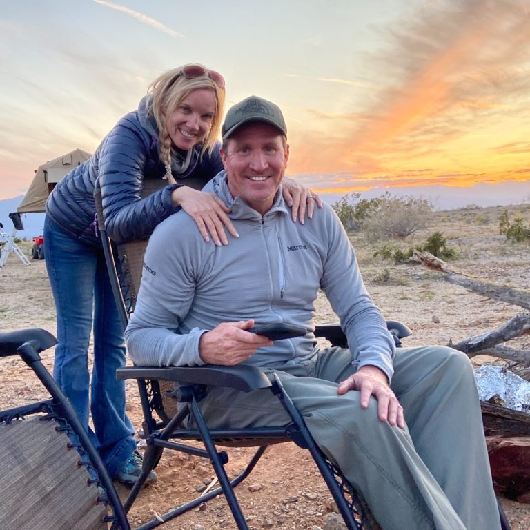 Memorial Video A man sitting in a chair with a woman standing behind him, both smiling against a sunset backdrop.