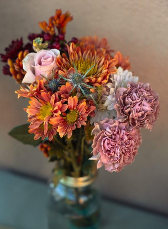A bouquet of colorful flowers in a glass jar, featuring roses and chrysanthemums.
