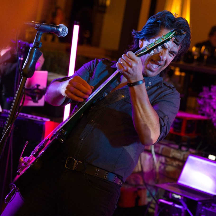 Man playing electric guitar passionately on stage during a live performance.