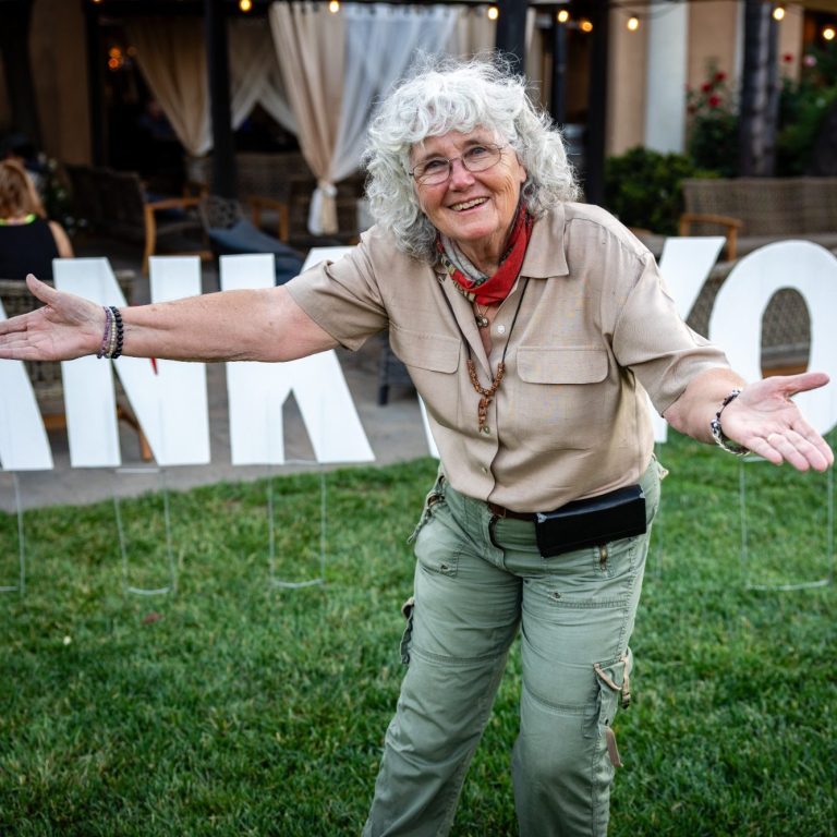 Reality Rally Smiling woman with curly gray hair gestures warmly in front of "THANK YOU" sign.
