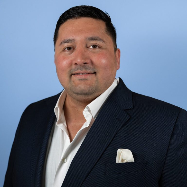 Business Headshot Man in a suit jacket with a white shirt and pocket square, smiling against a blue background.