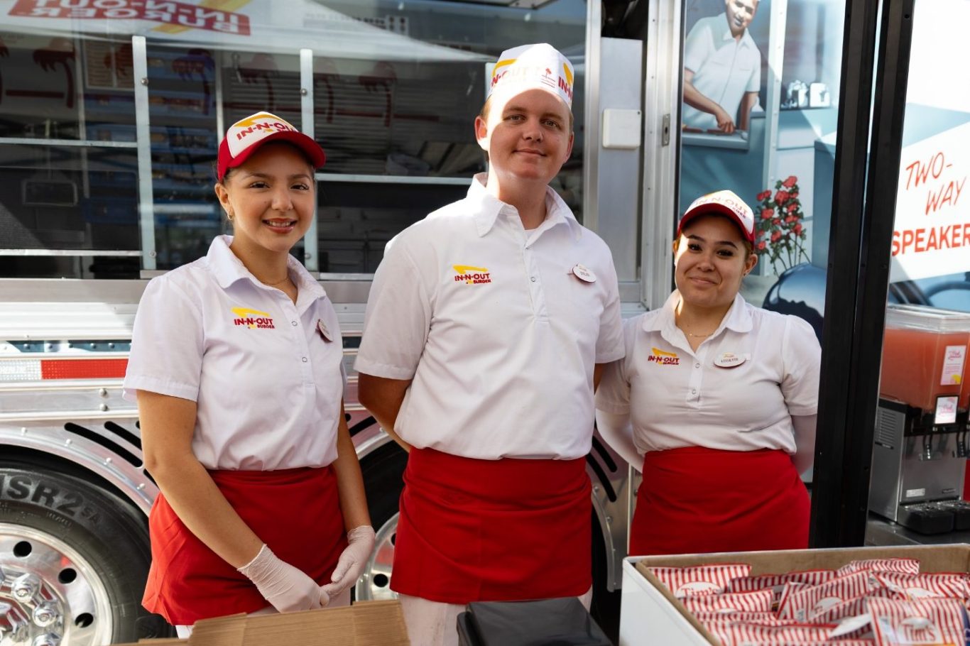Social media videos Three smiling food service workers in uniforms stand in front of a food truck.